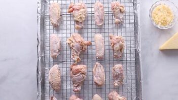 Chicken wings sit on a wire rack over a foil lined baking tray.