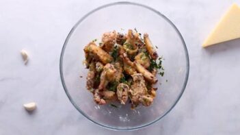 Golden crispy wings in a large glass bowl with minced parsley.