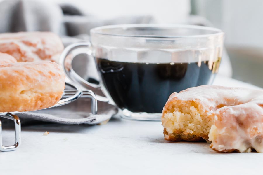 a bitten donut next to a cup of black coffee