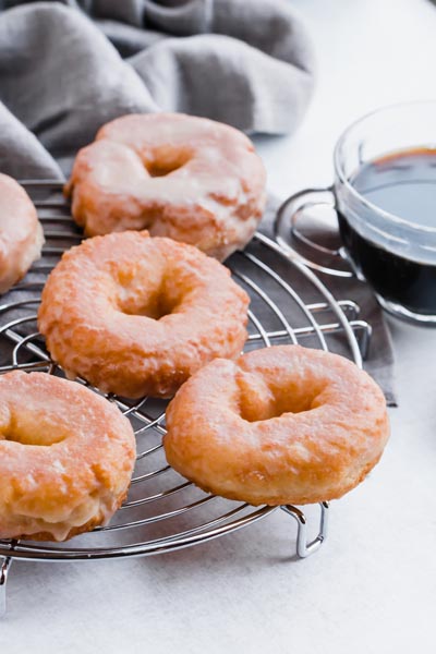 glazed cake donuts on a wire rack cooling next to a cup of black coffee