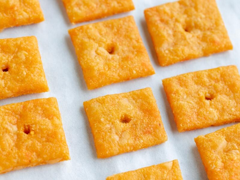 Baked gluten-free cheese crackers on a parchment lined tray all in a row.