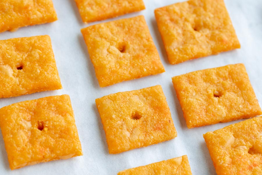 Baked gluten free cheese crackers on a parchment lined tray all in a row.