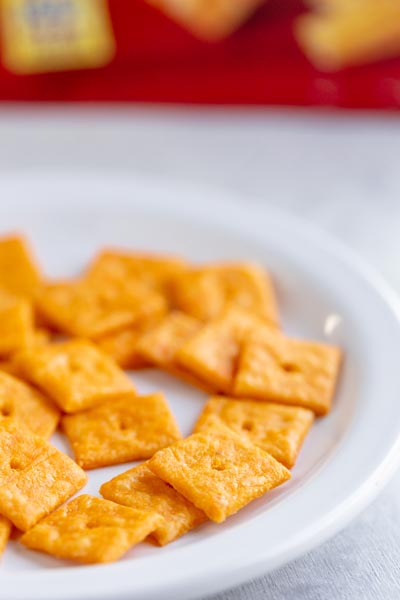 A plate of cheez it crackers in front of a red box of crackers.