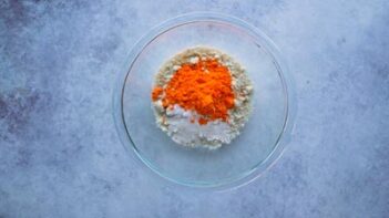 A glass bowl with dry ingredients and an orange powder inside.