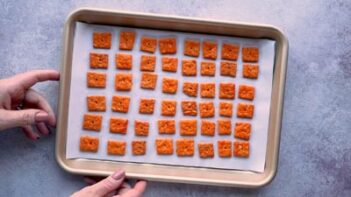 Hands holding a baking sheet with baked cheez-it crackers on it.