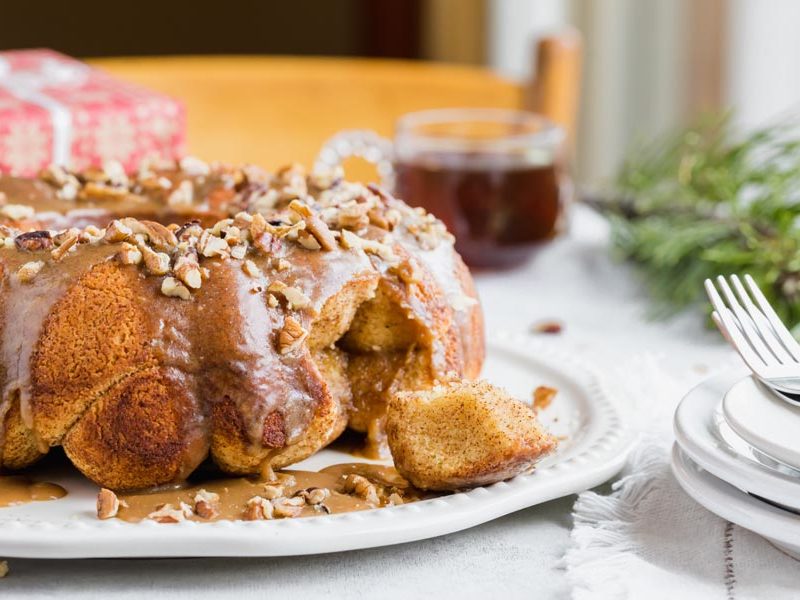 Glazed keto monkey bread with chopped pecans on a serving plate beside coffee and plates.