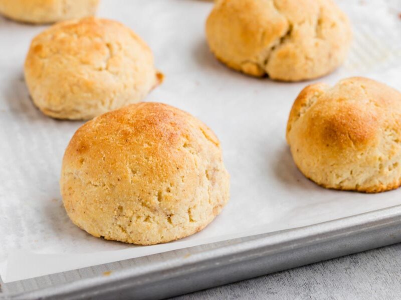 Freshly baked gluten-free yeast rolls cooling on a parchment-lined baking sheet.