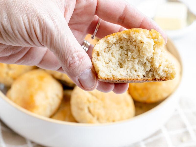 A hand holding a soft and fluffy gluten-free yeast roll with a bite taken out to show the texture.