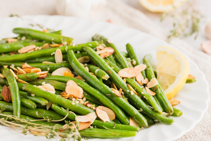 buttery green beans on a white platter with sliced almond, thyme and lemon slices