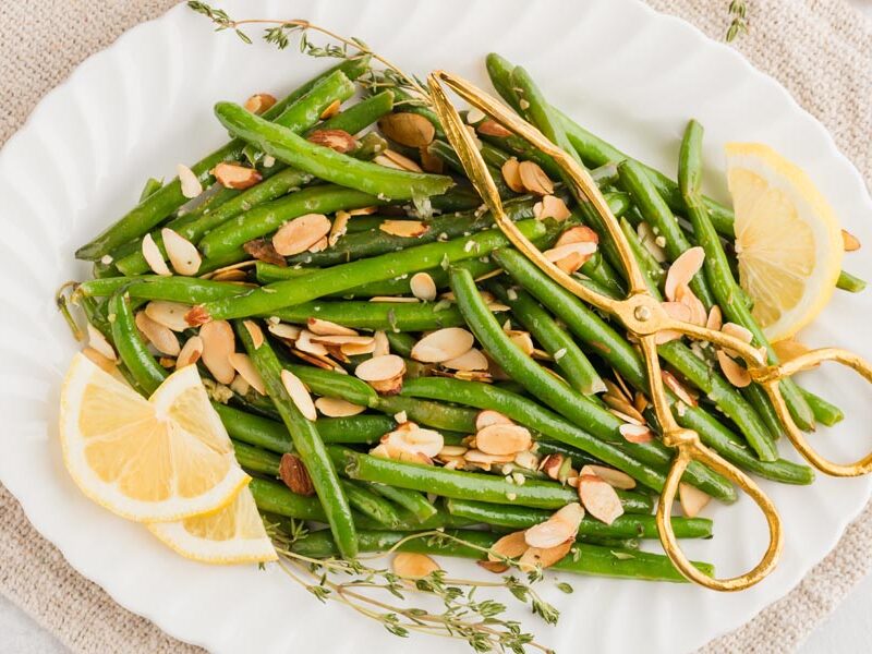 cooked green beans with almond on a platter with gold tongs