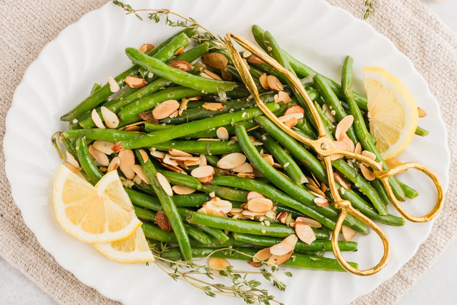 cooked green beans with almond on a platter with gold tongs