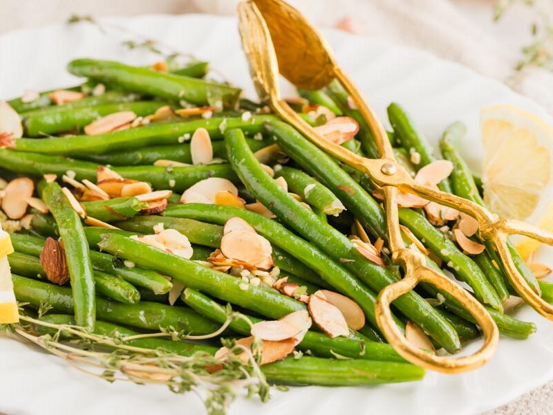 a plate of fresh green beans almondine with tongs on top of the beans