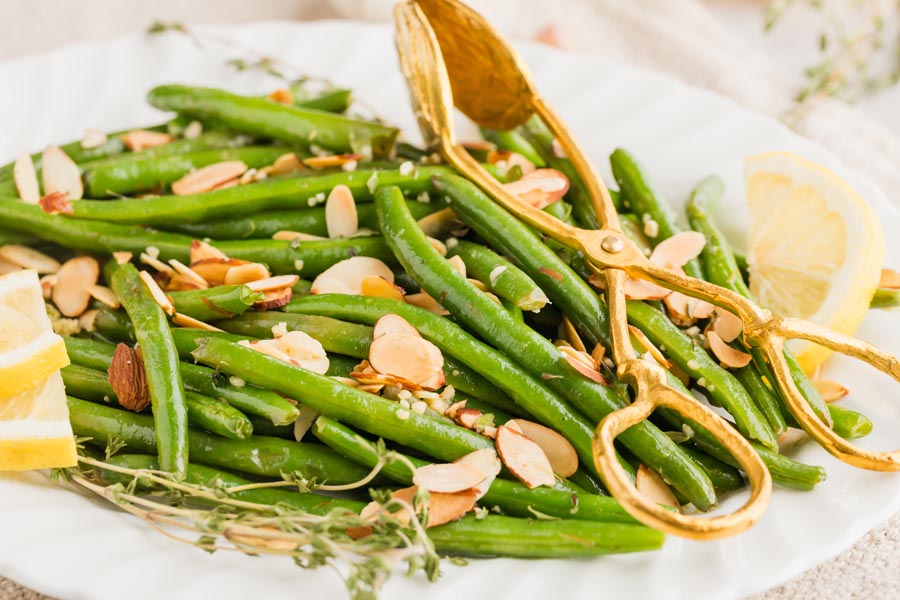 a plate of fresh green beans almondine with tongs on top of the beans