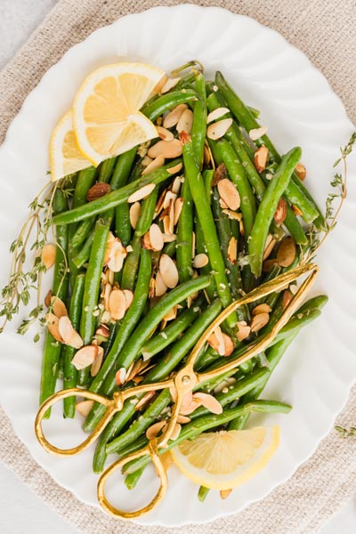 a white platter with green beans almondine and lemon wedges
