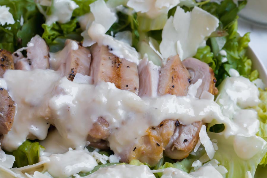 sliced grilled chicken with caesar dressing overhead shot