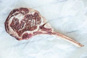 dry aged tomahawk steak with salt and peppercorns near by