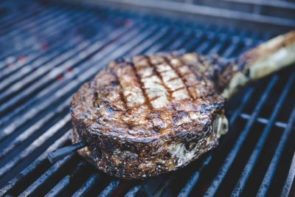 juicy ribeye steak cooking over the cold side of the grill