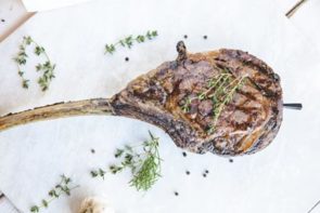 tomahawk steak resting on the counter with some herbs nearby