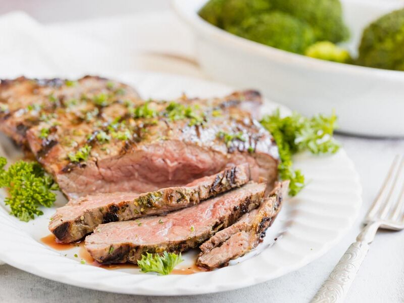 Sliced medium-rare flank steak with broccoli on a white platter.