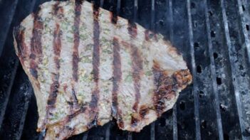 A piece of steak grilling on a gas grill.