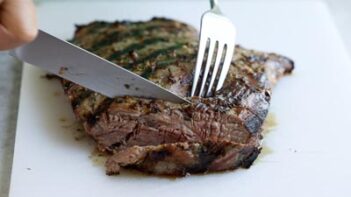 Slicing steak against the grain with a knife and fork.