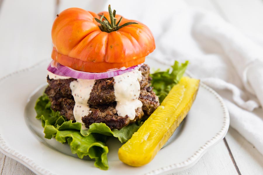 a bunless burger with a tomato slice on top and lettuce on the bottom with a side of pickle spear