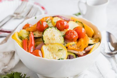 a bowl with cooked squash, tomatoes and peppers coated with chopped herbs