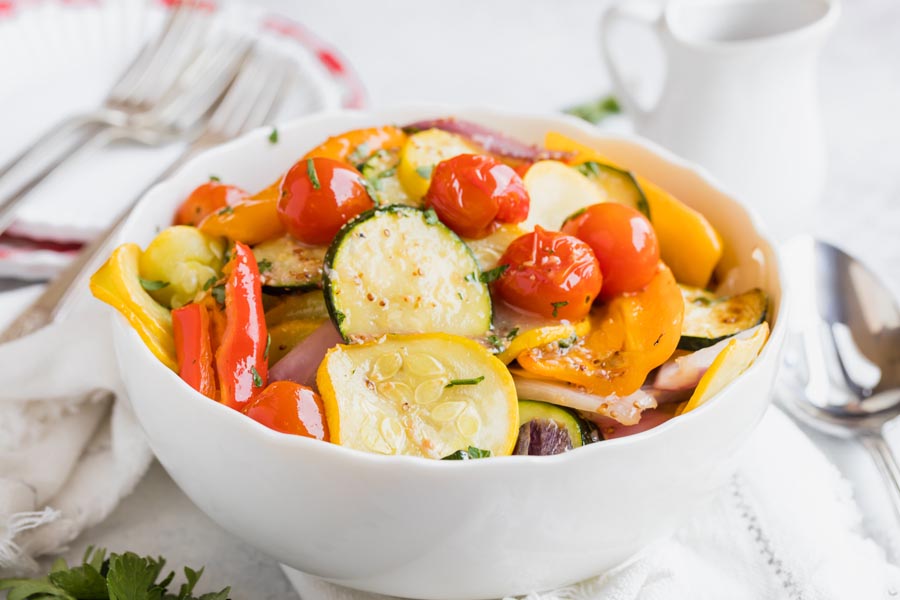 a bowl with cooked squash, tomatoes and peppers coated with chopped herbs
