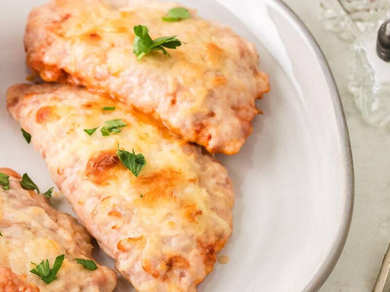 Baked ground chicken calzones topped with melted cheese and fresh parsley on a white serving plate.