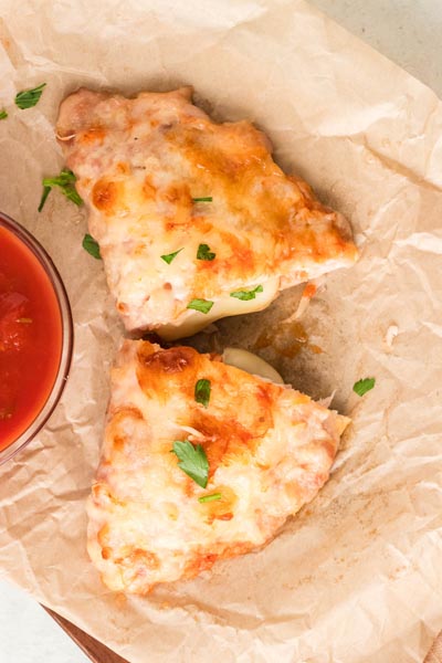 Two golden ground chicken calzones topped with melted mozzarella and parsley on parchment paper.