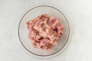 Ground chicken mixed with seasonings in a glass bowl to make zero carb calzone dough.