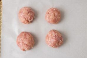 Seasoned ground chicken divided into four evenly sized balls on parchment paper.