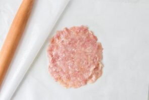 Ground chicken flattened into a thin round circle between sheets of parchment paper for a calzone crust.