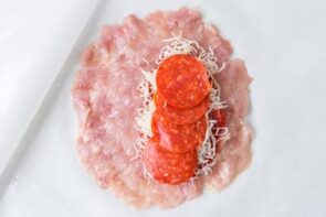 Flattened ground chicken topped with shredded mozzarella and pepperoni on one half before folding.