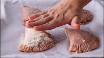 1. Ground chicken calzones being sealed around the edges and topped with grated Parmesan before baking.
