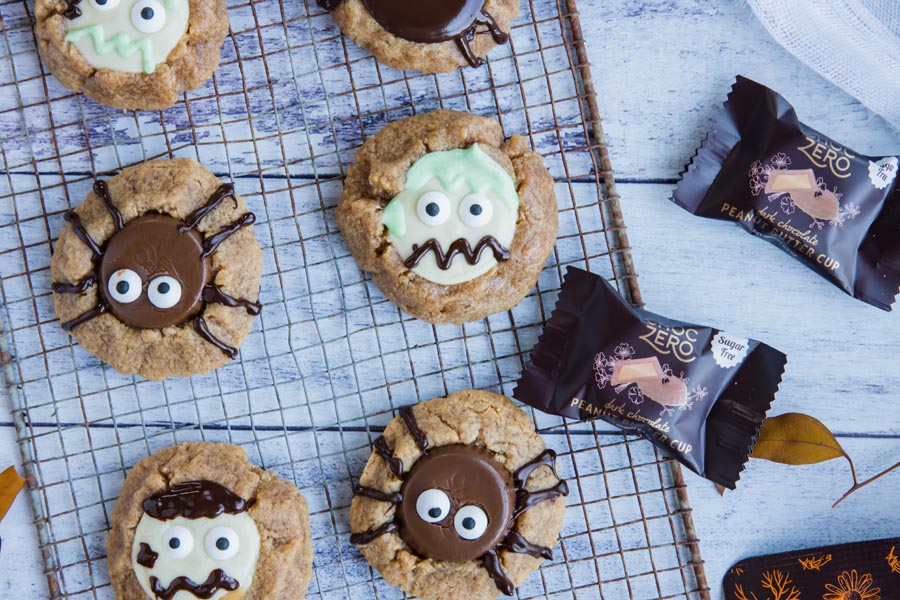 a wire rack with keto peanut butter cup cookies on it decorated like spiders and zombies