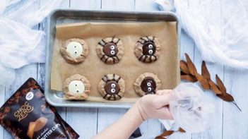 piping dark chocolate spider legs on spider cookies