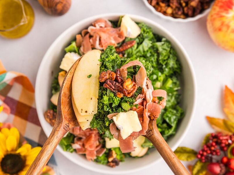 Salad tongs holding up a serving of harvest salad with nuts and apple.