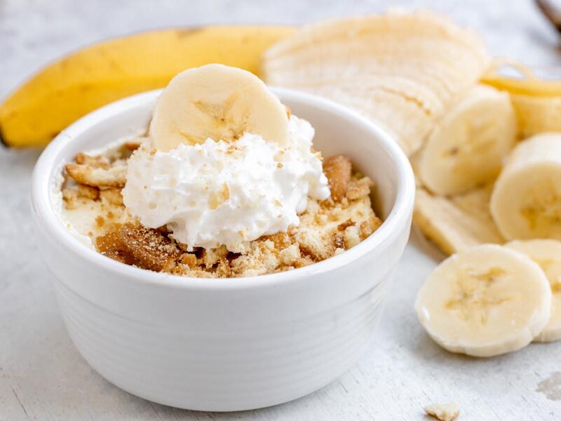 Easy healthy banana pudding in a white bowl topped with sugar-free vanilla wafers, whipped cream and a banana slice.