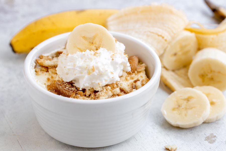 Easy healthy banana pudding in a white bowl topped with sugar-free vanilla wafers, whipped cream and a banana slice.