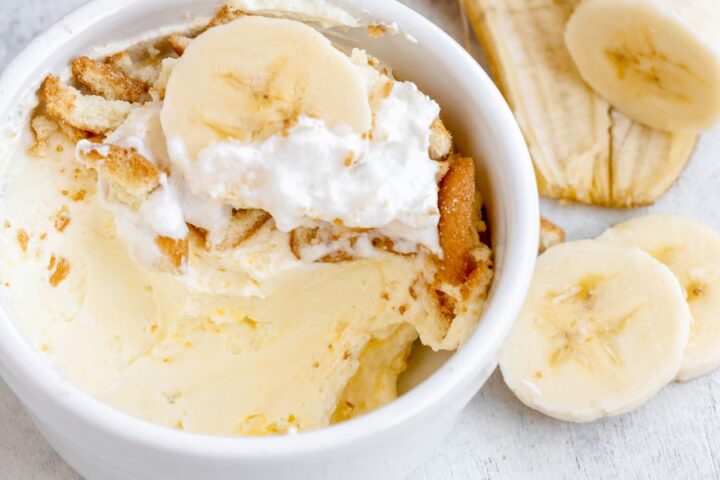 Close up of banana pudding in a white bowl and a sliced banana on top.