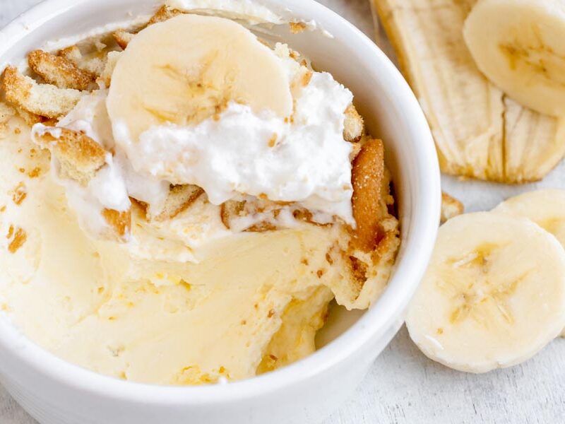 Close up of banana pudding in a white bowl and a sliced banana on top.
