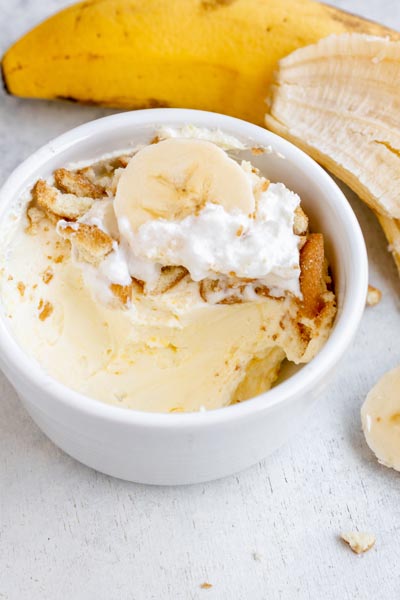 A bowl with a few bites of banana pudding missing and topped with cookies and whipped cream.