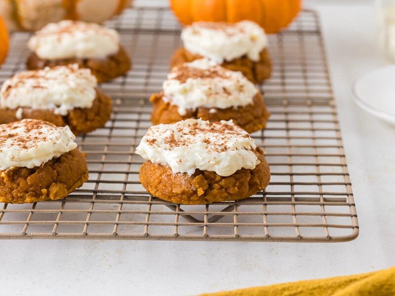 Frosted pumpkin cookies dusted with cinnamon on a wire cooling rack.