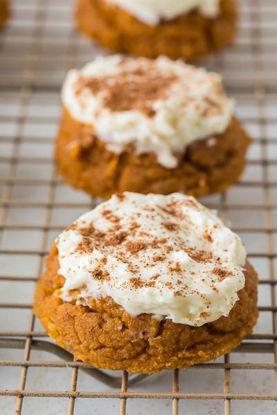 Close-up of a single pumpkin cookie on a cooling rack with fluffy frosting and sprinkled cinnamon.
