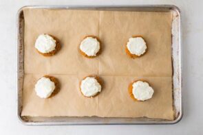 Freshly baked pumpkin cookies topped with cream cheese frosting rest on a parchment-lined baking tray.
