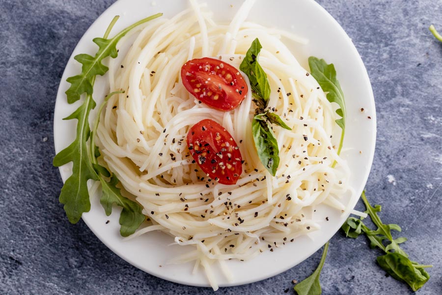 a plate of noodles topped with basil, tomatoes and cracked pepper