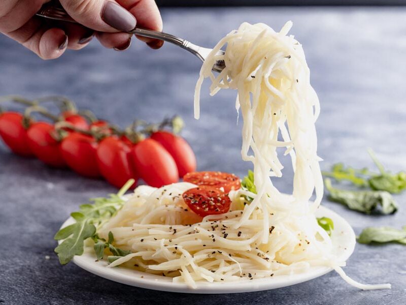 holding a forkful of noodles over a plate of more noodles