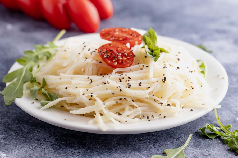 a plate with noodles topped with black pepper, basil, lettuce and cherry tomatoes