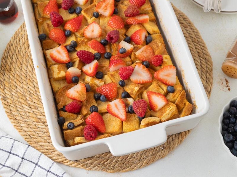 A white casserole dish filled with french toast casserole and topped with fresh berries.